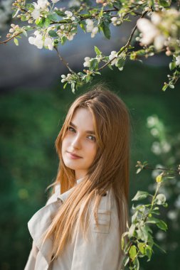 Uzun bej yağmurluklu güzel bir kız güneşin tadını çıkarıyor..