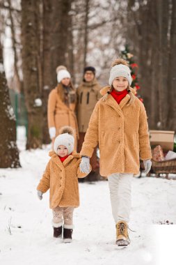 Küçük kız kardeşimle kış parkında kar ve çam ağaçlarının arasında yürüyoruz..
