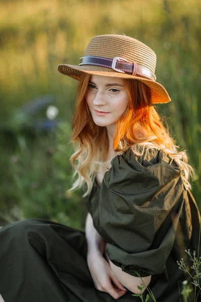 Kızıl saçlı genç bir kız karahindibaların arasında çayırda oturuyor..