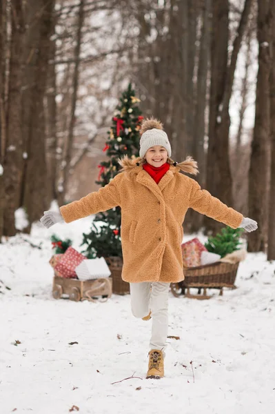 子供たちは冬の雪に覆われた森の中で装飾されたクリスマスツリーの隣でプレゼントで遊ぶ — ストック写真