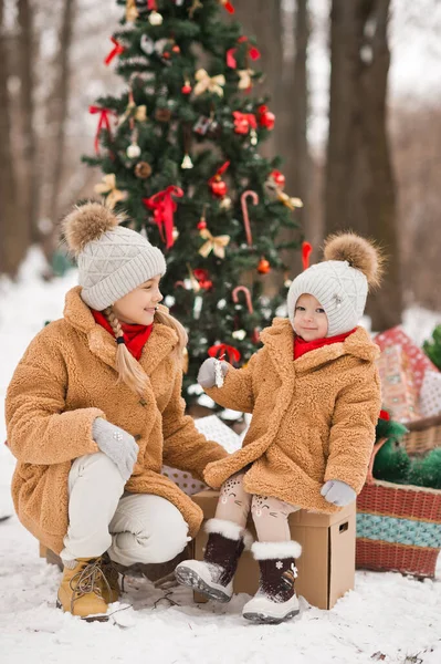 子供たちは冬に森の中に風船でクリスマスツリーの近くの贈り物に座っています — ストック写真