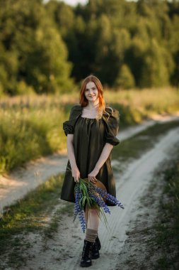 Köylü kızıl saçlı bir kız yazın kırsal bir yolda yürüyor..