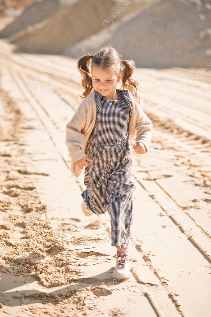 A little girl runs happily among the sand.