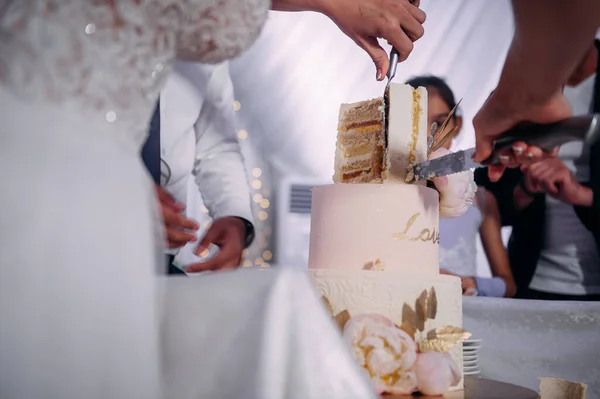The hands of the newlyweds cut the cake into pieces.