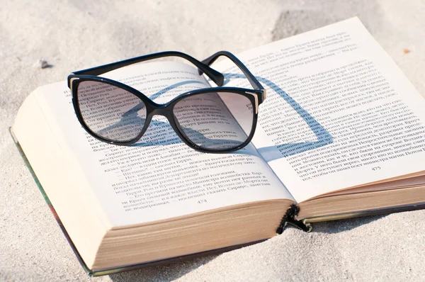 Βιβλίο και γυαλιά ηλίου σε μια παραλία με άμμο — Φωτογραφία Αρχείου