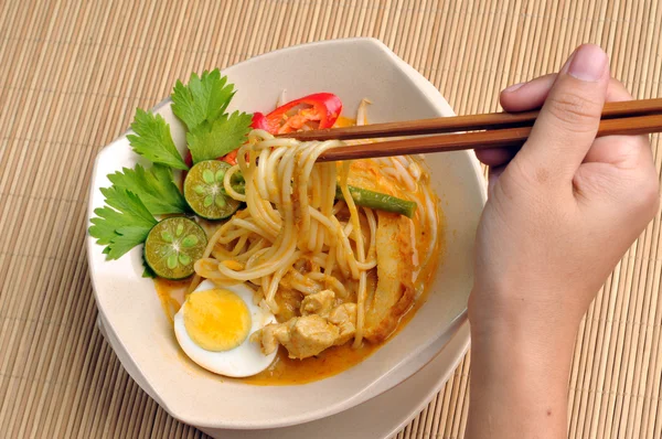 Crooped view of hand holding chopstick to eat curry noodles