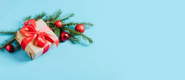 Festliche Schachtel mit roter Schleife auf blauem Hintergrund mit weihnachtlichen Spielzeugkugeln aus flauschigen Fichtenfunkeln und Konfetti. Neujahrskonzept. Flache Festmockup mit Kopierraum — Stockfoto