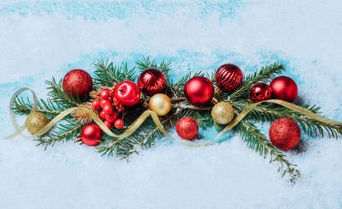 Noel çelengi kırmızı ve altın Noel topları, çelenk, tüylü köknar dalları, mavi arka plan, kar taneleri, ışıltılı konfeti.