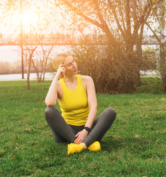 Una mujer en ropa deportiva está descansando después de hacer deporte o yoga en la calle de la ciudad. Un estilo de vida activo y saludable en la ciudad moderna — Foto de Stock