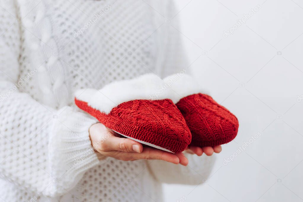 Woman in white sweater holds warm knitted red slippers. Concept of home family cozy holiday Christmas New Year.
