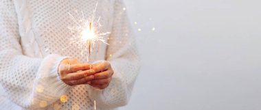 Beyaz kazaklı bir kız yanan maytap tutuyor. Yılbaşı partisi Noel tatili konsepti. ışık arkaplanı, kopyalama alanı