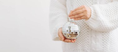 Beyaz kazaklı bir kız elinde parlak bir disko topu Noel oyuncağı tutuyor. Yılbaşı partisi konsepti.