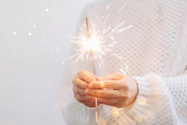 Beyaz kazaklı bir kız yanan maytap tutuyor. Yılbaşı partisi Noel tatili konsepti. ışık arkaplanı, kopyalama alanı