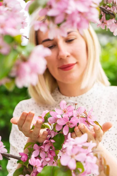 Genç bir kadın elinde çiçek açan bahar çiçekleriyle bir dal tutuyor. Bahar parkı ya da bahçe, çiçek açan ağaçlar.