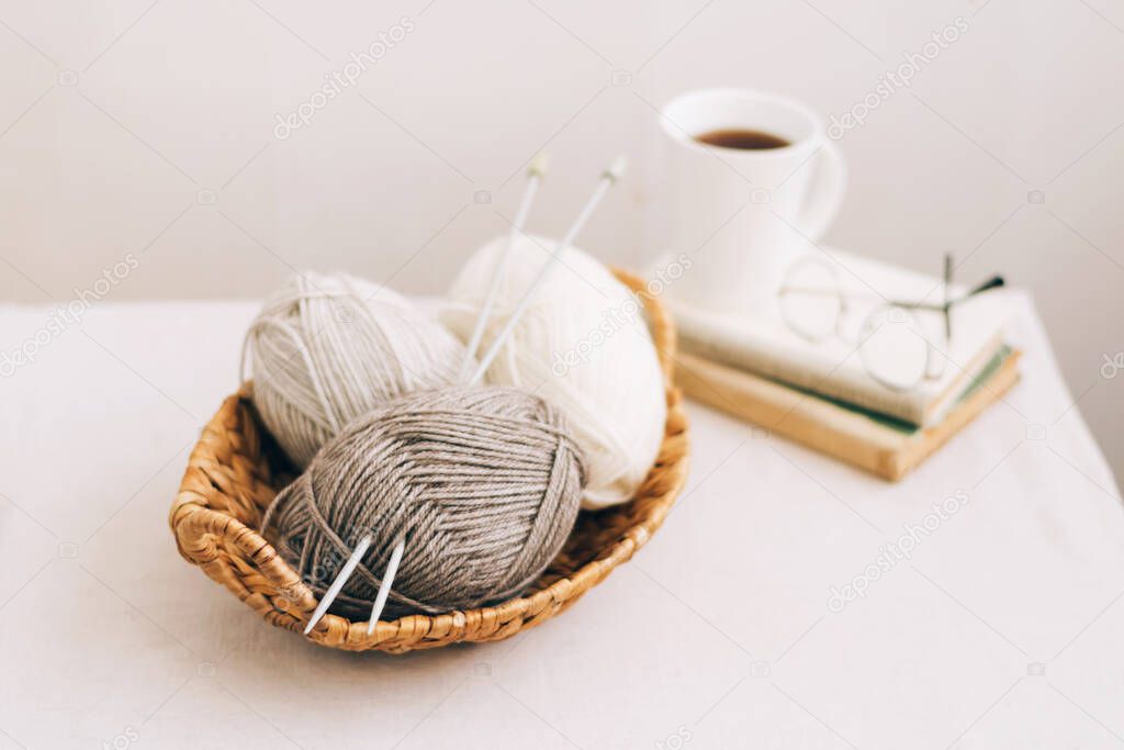 Natural wool in balls of various pastel colors in a wicker basket. Knitting threads close-up on a light background.