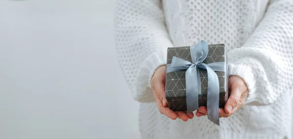 As mãos femininas estão segurando uma pequena caixa de presente. Férias de inverno conceito Ano Novo Natal. Foco seletivo, fundo claro — Fotografia de Stock