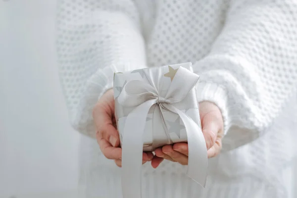 Kadın eli küçük bir hediye kutusu tutuyor. Kış tatili konsepti yılbaşı. Seçici odak, ışık arkaplan — Stok fotoğraf