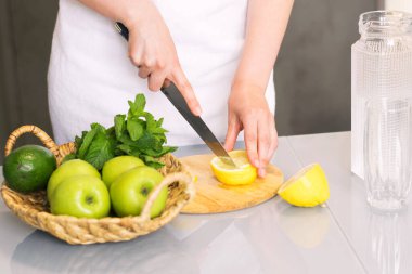 Evde mutfakta limonlu ve naneli arınma içkisi yapan bir kadın. Canlandırıcı su limonu, antioksidan.
