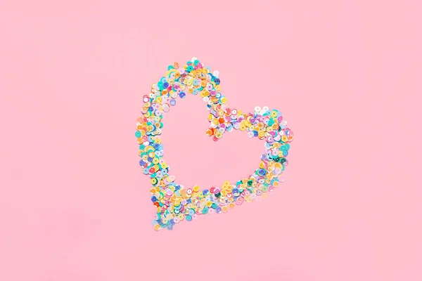 Coração feito de confetes de lantejoulas multicoloridas sobre fundo rosa. Espaço de cópia de composição festiva plana — Fotografia de Stock