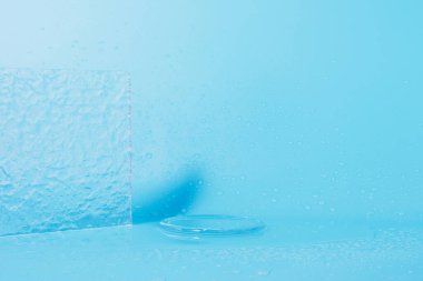 Şeffaf cam ve su damlalarıyla mavi arka plan. Kozmetik ürünleri için boş podyum.