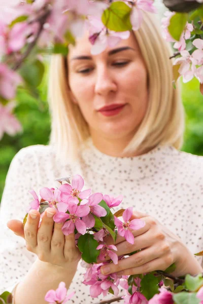 Una mujer joven sostiene una rama con flores florecientes de primavera en sus manos. Parque natural o jardín de primavera, árboles con flores — Foto de Stock
