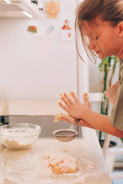 Nettes Teenager-Mädchen in Küchenschürze bereitet und knetet Produkte für die Teigzubereitung zum Backen Stockbild