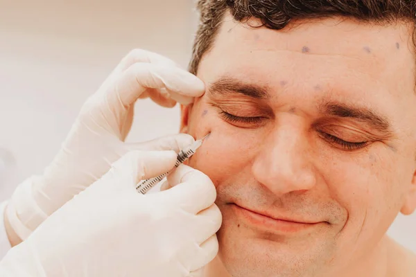 Kosmetologe führt Verjüngung Verfahren setzt Botox-Injektion auf den Menschen. Das Konzept verjüngender Behandlungen lizenzfreie Stockbilder
