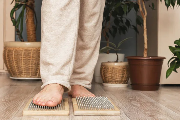 Frau steht auf Nägeln vor dem Hintergrund heimischer Grünpflanzen. Die Praxis, auf Nägeln zu stehen. Stockfoto