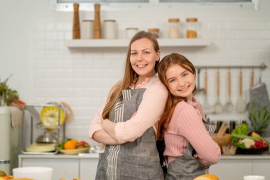 Beyaz kadın ve kızı önlük giyer ve yan yana dururlar. Ayrıca yemek pişirirken kameraya bakıp gülümserler..