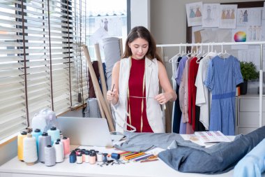 Genç profesyonel tasarımcı ya da terzi kadının geniş açılı görüntüleri ev ofisinde farklı aksesuarlarla çalışmak için mezura kullanıyor ve mutlu görünüyor..