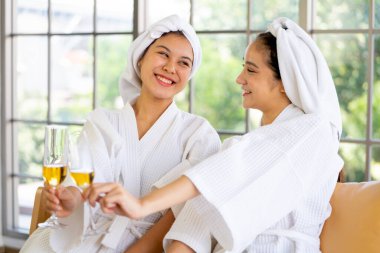 Spa cüppeli iki Asyalı güzel kadın ellerinde şarap bardakları ve hareketleriyle spa masajından sonra birlikte eğleniyorlar ve gün ışığında resepsiyon odasında kalıyorlar..