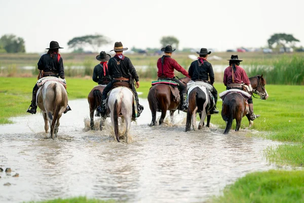 Back of group of cowboy and cowgirl ride horse through water in reservoir with day light.