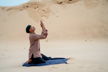 Müslüman adam oturur ve gün ışığıyla çölün kumlarında dua eder..