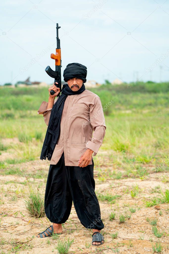 Terrorist man with veil stand and hold gun also look at camera to prepare for fight with the enemy in grass field and day light.
