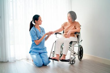 Asyalı genç hemşire yaşlı bir kadının yanında oturuyor ve kadınları hastalıktan kurtarmak için el ele tutuşuyorlar ve beyaz perdenin önünde oturma odasında kalıyorlar..