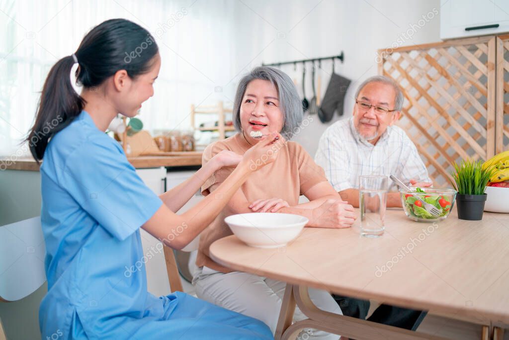 Nurse or doctor who work as homecare staff help to serve a spoon of mush rice to senior woman with her husband sit beside.