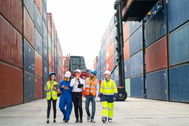 Profesyonel mühendis, işçi ya da teknisyen grubu, arka planda vinç ve konteynır deposu olan kargo konteynır işyeri alanındaki işleri birlikte tartışır ve tartışır..