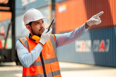 Asyalı profesyonel kargo konteynırı işçisi veya teknisyeni iş arkadaşı ile iletişim kurmak için telsiz ya da telsiz kullanıyor.