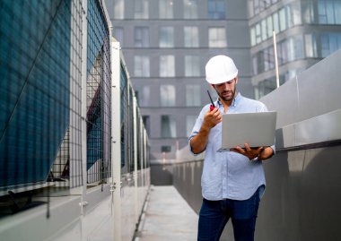 Profesyonel mühendis ya da teknisyen, projenin çözümü hakkında iş arkadaşıyla iletişime geçmek ve yüksek binanın terasında kalmak için dizüstü bilgisayar ve telsiz kullanıyor..