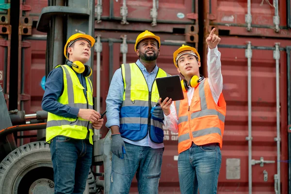 Asian cargo container worker or staff hold tablet and point to explain to African American technician in workplace area.