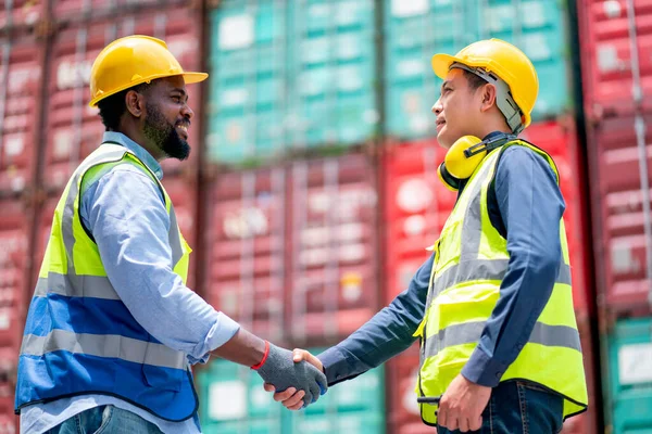 African American worker or technician shake hands with Asian staff in cargo container workplace area with stack of container tank as background.