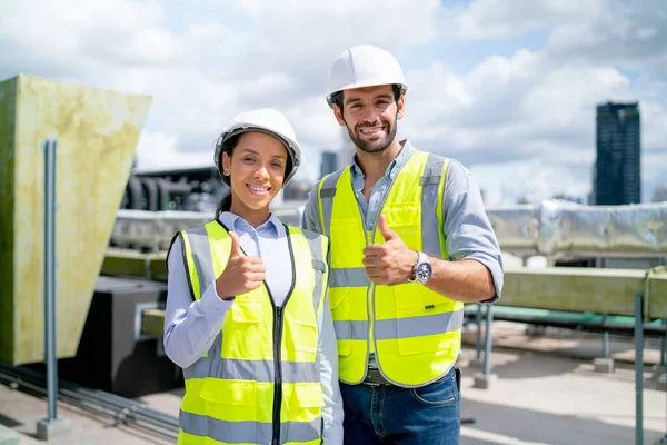 Portrait of two professional engineer or technician workers stand and look at camera with smiling and show thumbs up on terrace of construction site and day light.