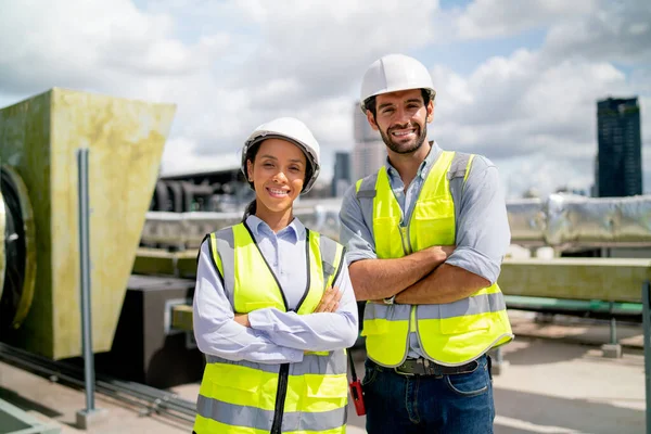 Portrait of two professional engineer or technician workers stand and look at camera with smiling and arm-crossed on terrace of construction site and day light.