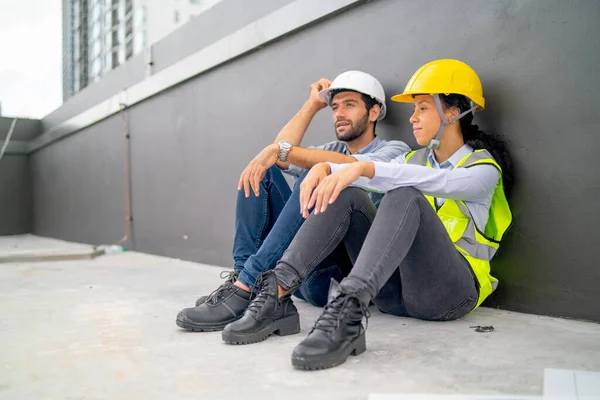Couple professional engineer or technician sit on the floor of terrace of construction site during relax after work and talk together and they look happy.