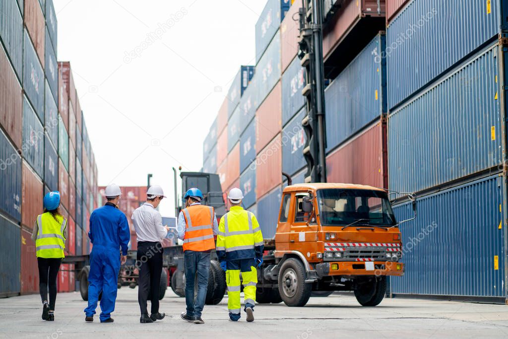 Back of professional engineer, worker or technicians walk and discuss together about work in cargo container workplace area with crane, truck and stack of container tank on background.