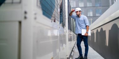 Geniş açılı profesyonel mühendis ya da teknisyen inşaat sahasının terasında makinenin yanında duruyor ve ekipmanların işlevini kontrol ediyor..