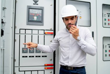 Different actions and working of engineer man hold walkie talkie and sometime use to contact his coworker and stay in front of electrical control panel.