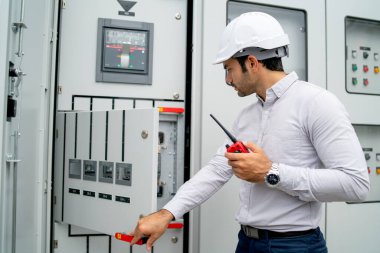 Different actions and working of engineer man hold walkie talkie and sometime use to contact his coworker and stay in front of electrical control panel.