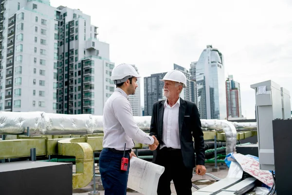 Wide shot of two engineer or technician worker shake hands together for successful of project and they stay on rooftop of construction site.