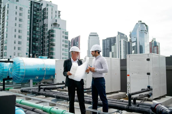 Wide shot of two engineers or technician man discuss together using building plan or drawing and they also stay on rooftop area of construction site.
